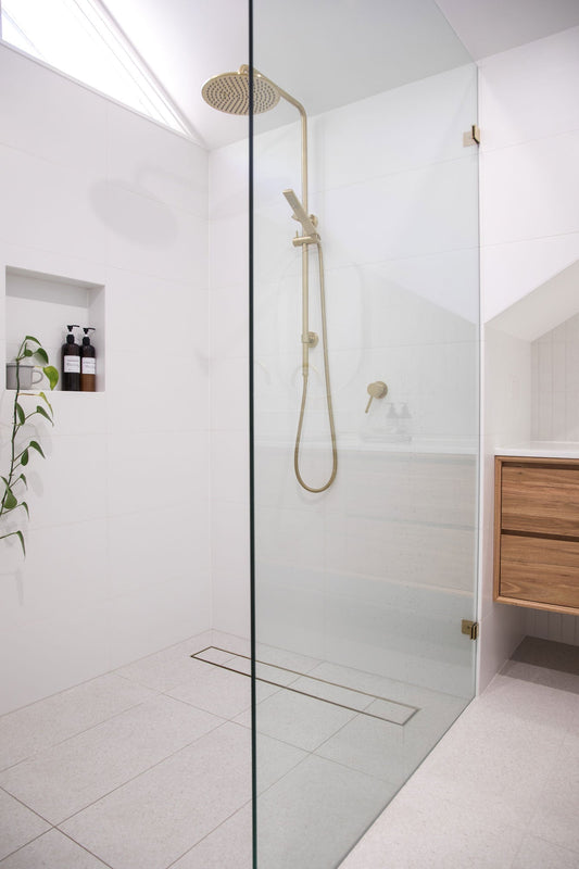 Brass tile insert drain in minimalist white bathroom.